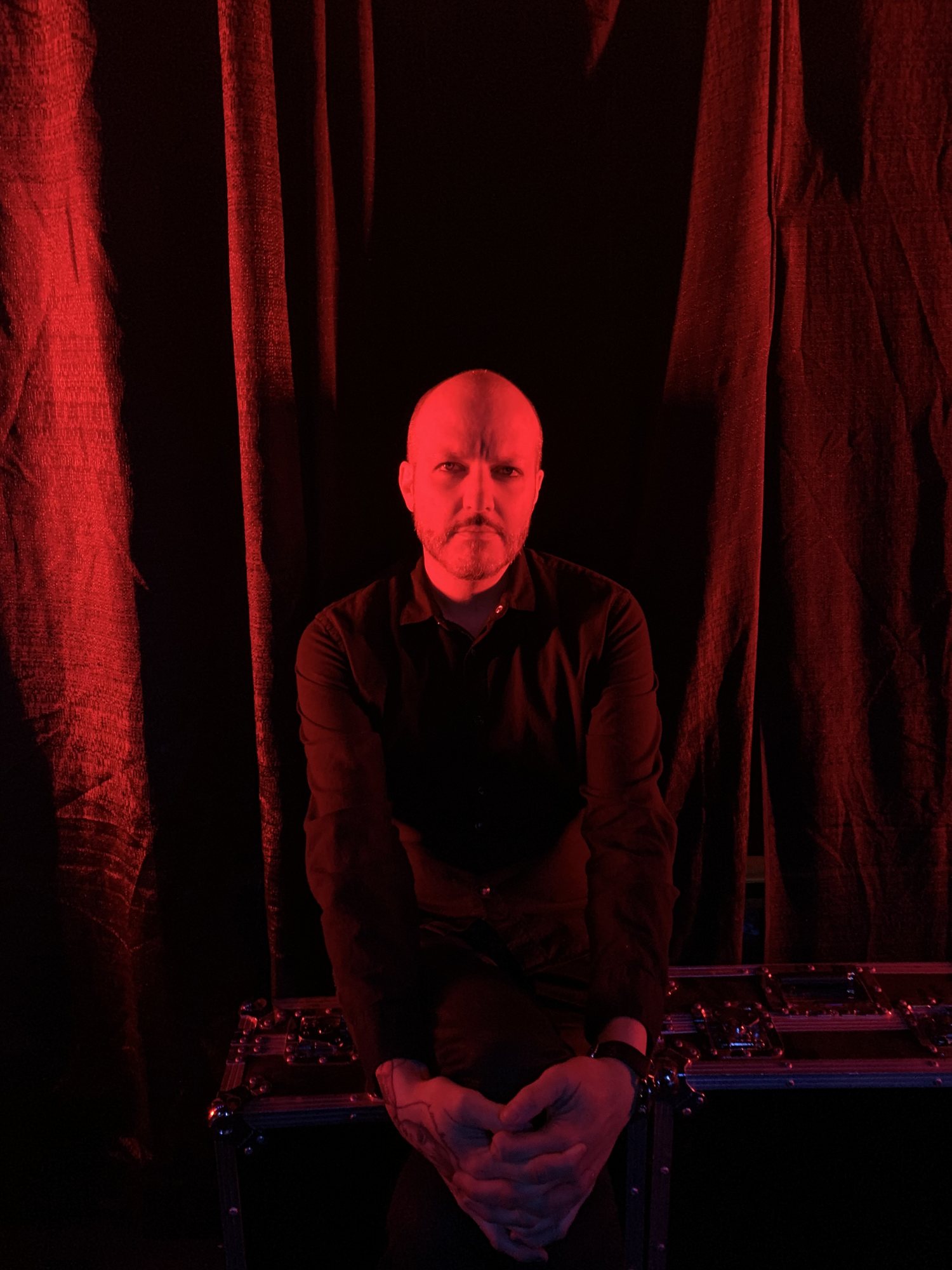 DJ Boyhollow, lit in red, seated in front of red curtains
